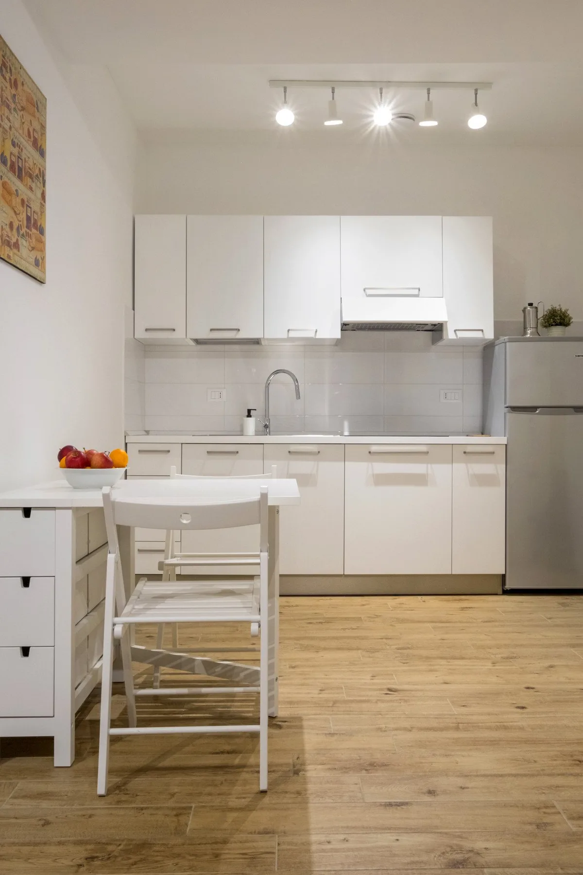 A bright kitchen with white cabinets, a dining table, and wood-look flooring.