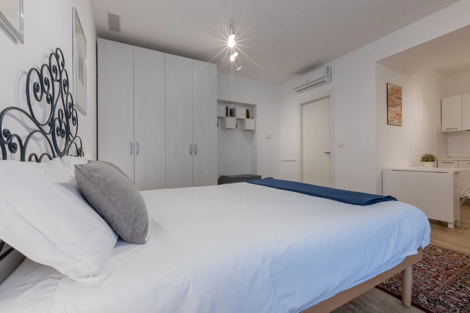 A bedroom with a large bed, white wardrobes, and a small kitchenette.
