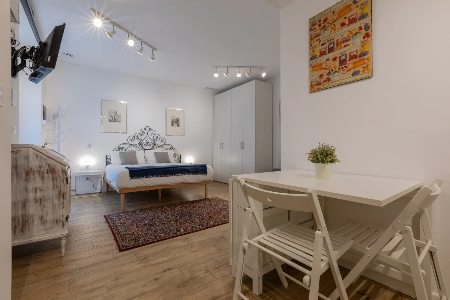 A bright bedroom with a bed, a white wardrobe, and a dining table.