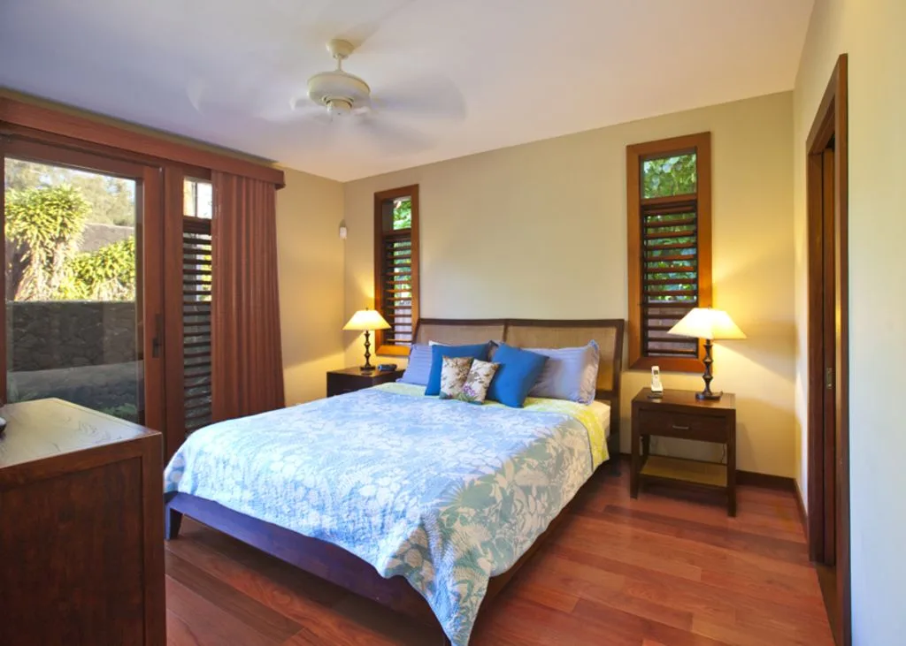 A bedroom with a bed, bedside tables, and windows overlooking greenery.