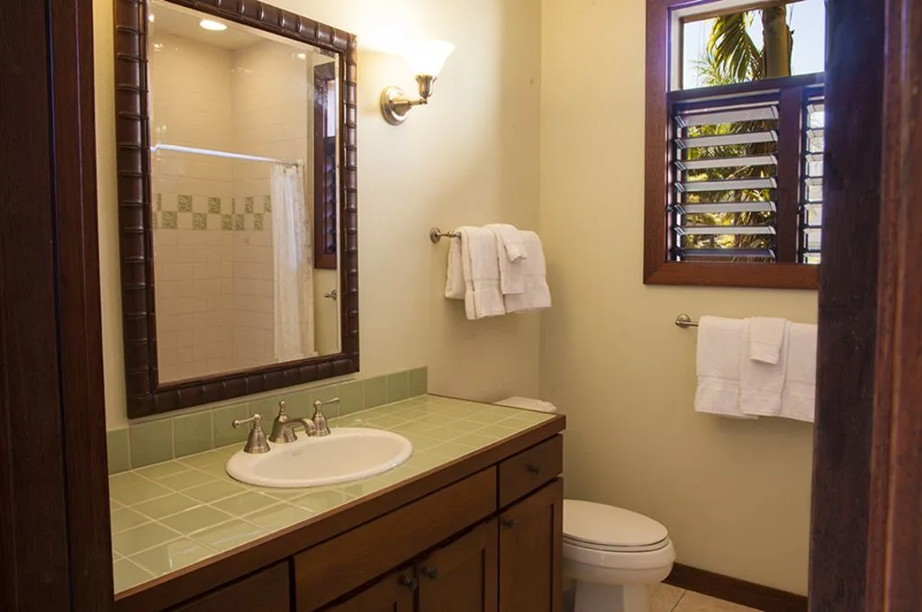 A bathroom with a tiled vanity, mirror, toilet, and window.