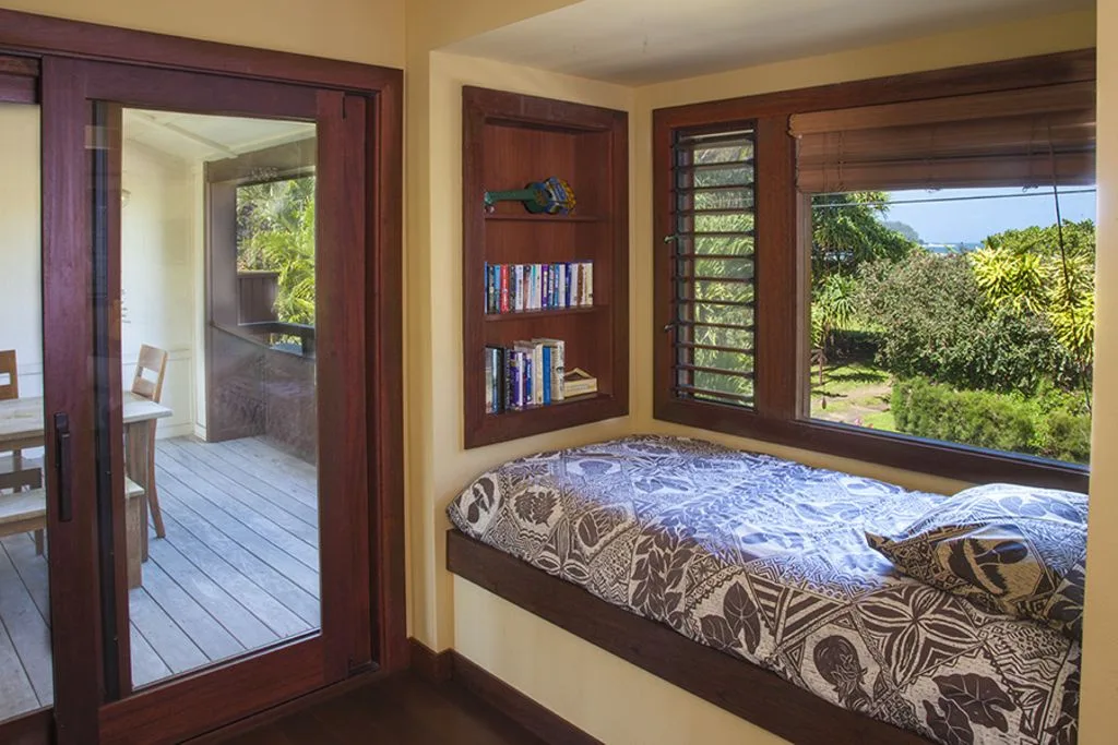 A bedroom with a bed beside a large window overlooking greenery.