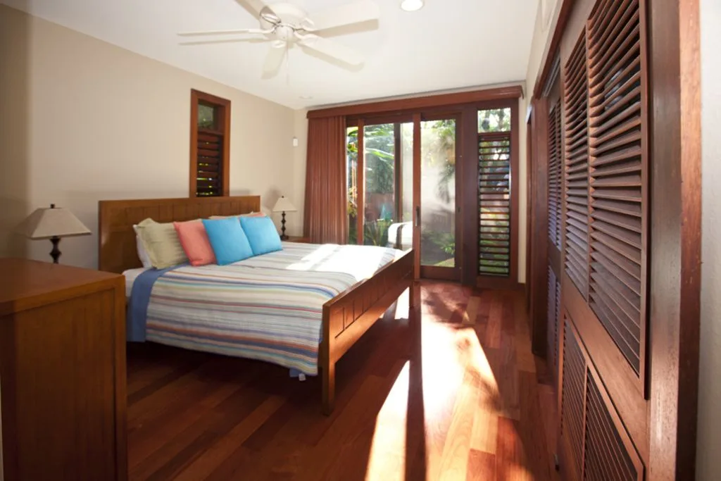A bedroom with a bed beside wooden shutters and glass doors.