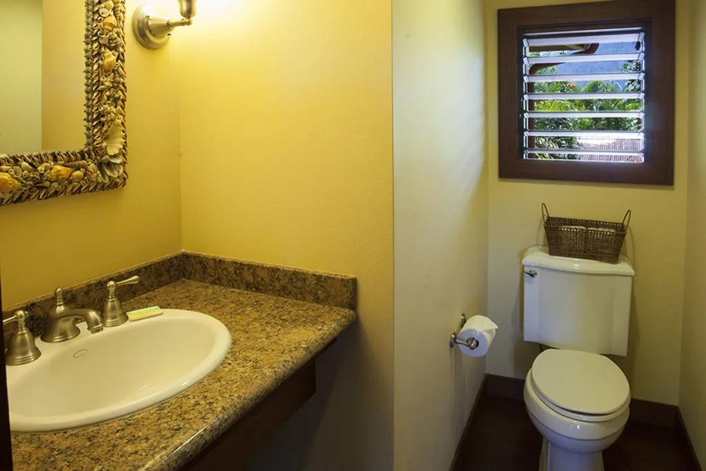 A bathroom with a sink, countertop, and toilet beneath a window.