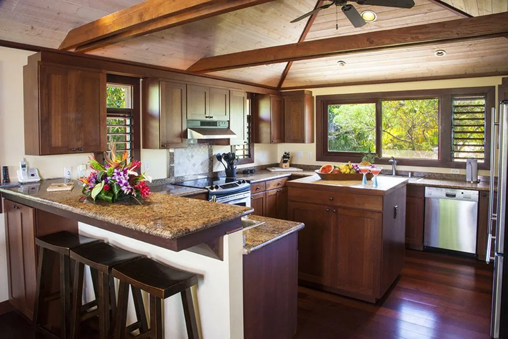A spacious kitchen with dark wood cabinets, stone counters, and large windows.