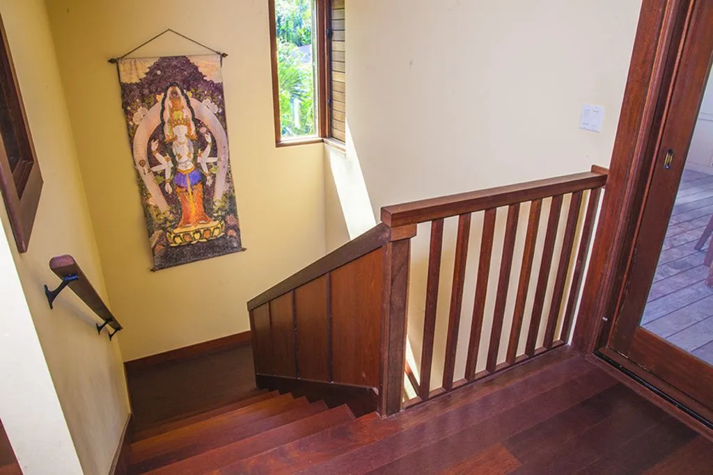A wooden staircase descends beside a railing and a colorful wall hanging.