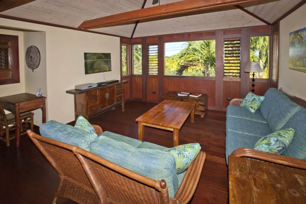 A living room with cushioned seating, wooden tables, and large windows overlooking greenery.