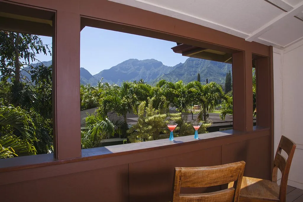 A covered patio overlooks lush greenery and mountains, with drinks on the ledge.
