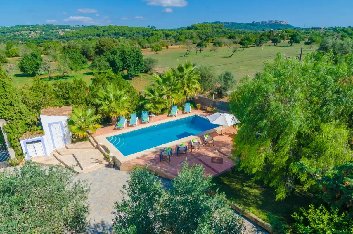 An outdoor pool and patio sit among trees, with open green fields beyond.