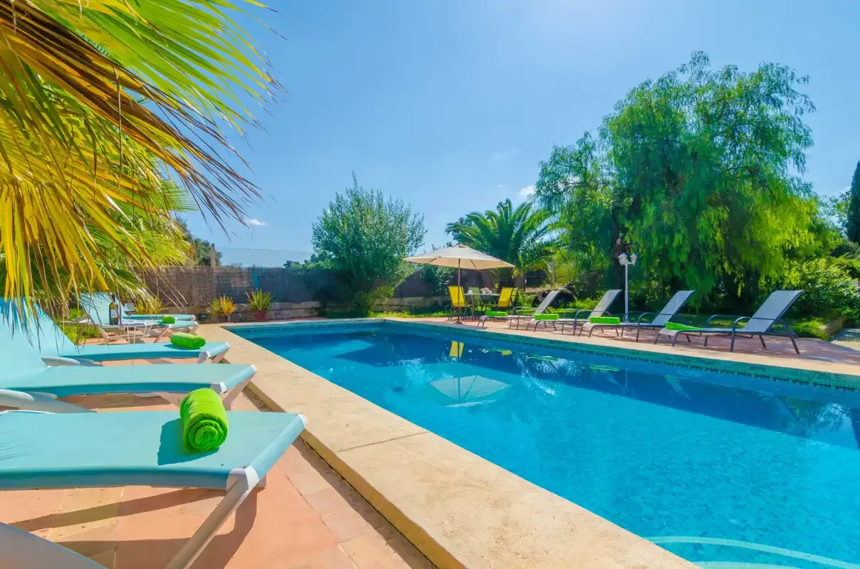 An outdoor swimming pool is surrounded by sun loungers and greenery.