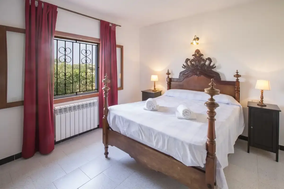 A bedroom with a large bed, bedside tables, and a curtained window.