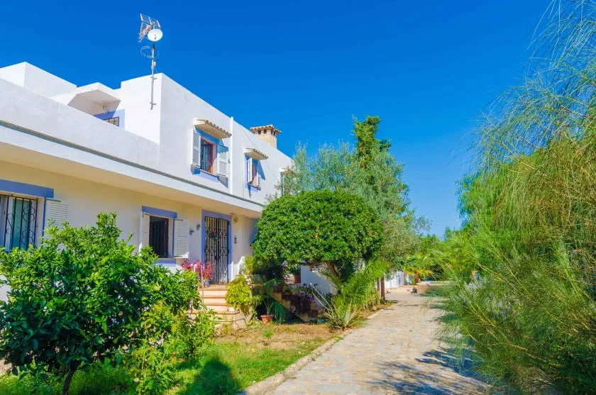 A white building stands beside a sunlit path bordered by greenery.