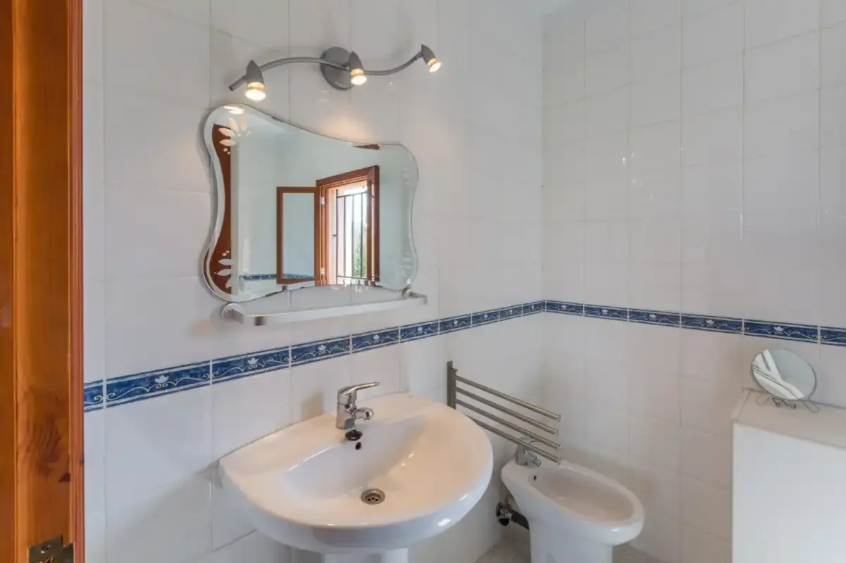 A tiled bathroom with a sink, mirror, and bidet.