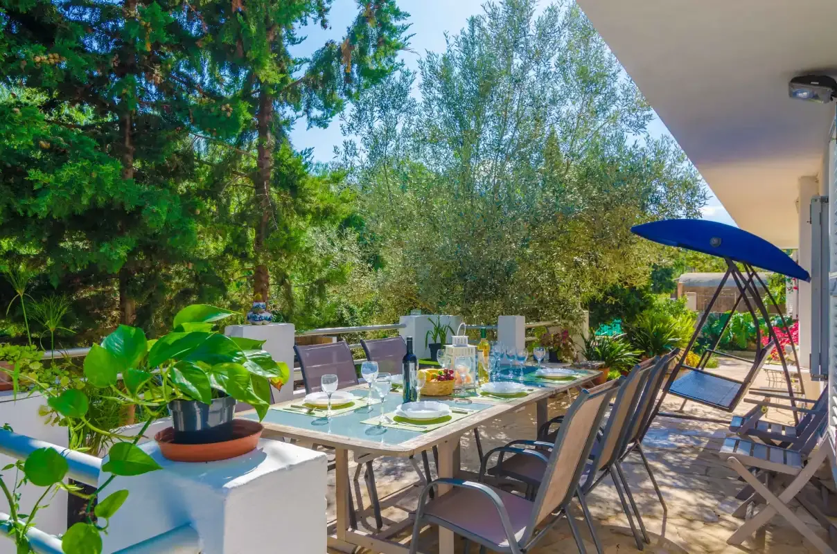 A shaded outdoor dining area with a table and seating among leafy trees.