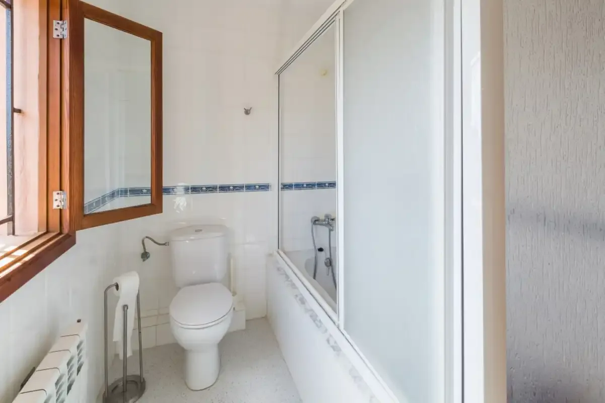 A bathroom with a bathtub, shower, toilet, and open window.