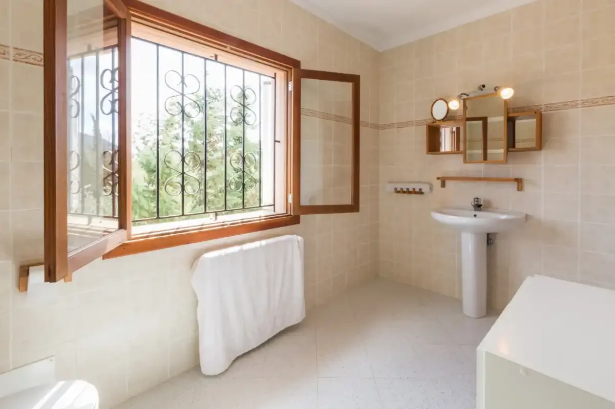A tiled bathroom with a sink and an open window.