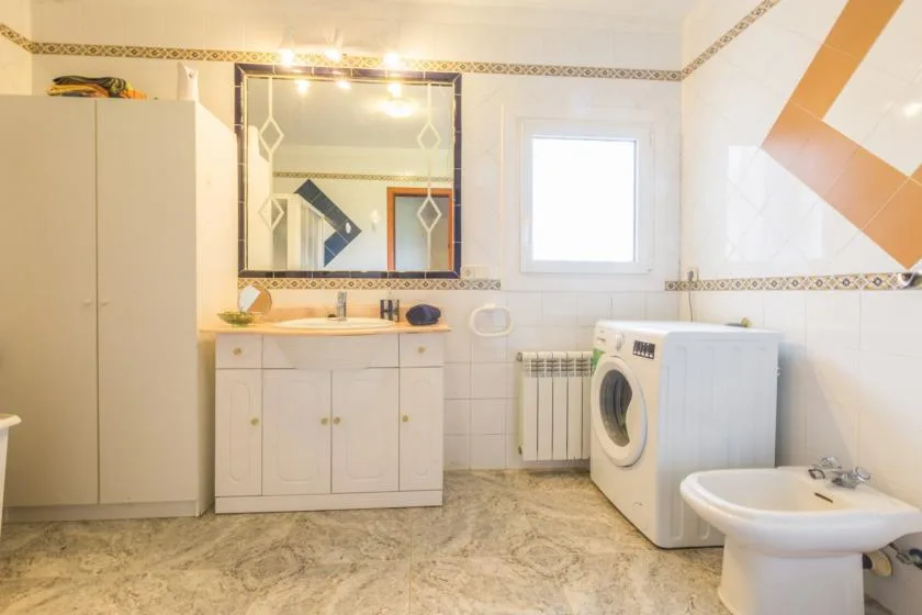 A bright tiled bathroom with a sink, mirror, and washing machine.