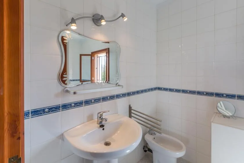 A tiled bathroom with a sink, mirror, and toilet.