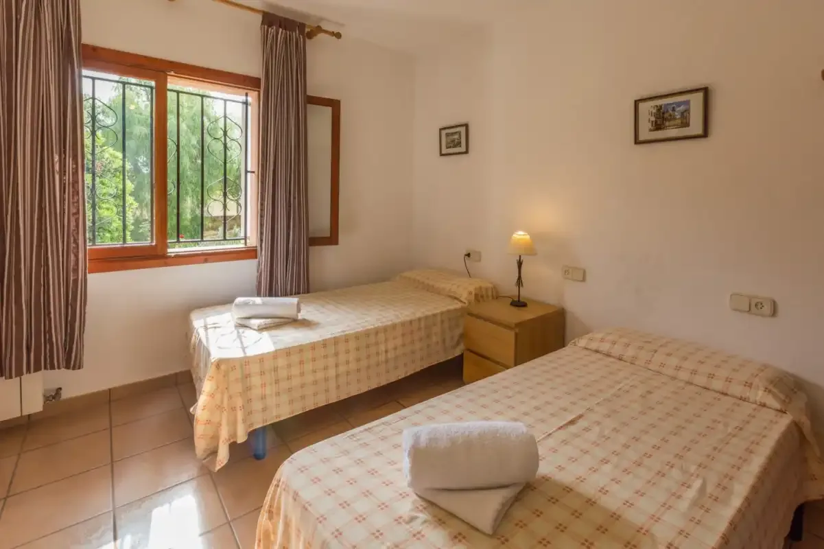A bedroom with two single beds, a window, and bedside furniture.
