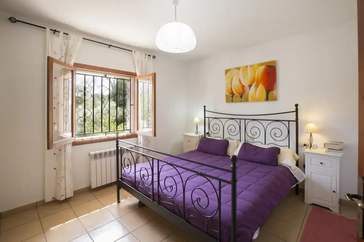 A bedroom with a purple bedspread, bedside tables, and an open window.