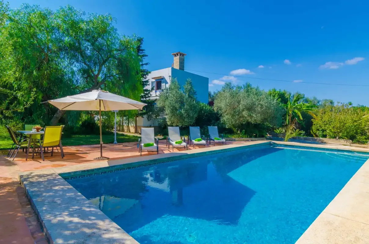 An outdoor swimming pool beside a patio with lounge seating and an umbrella.