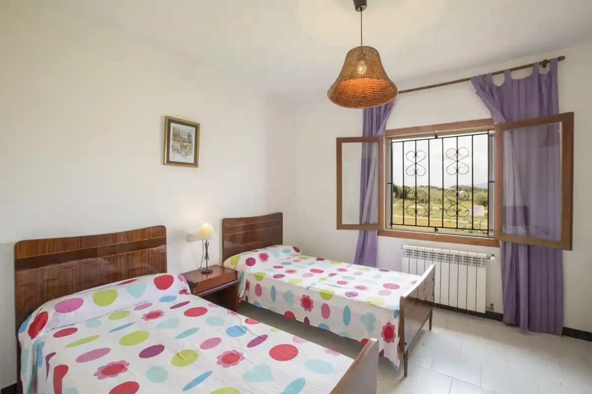 A bedroom with two beds beside a window with purple curtains.
