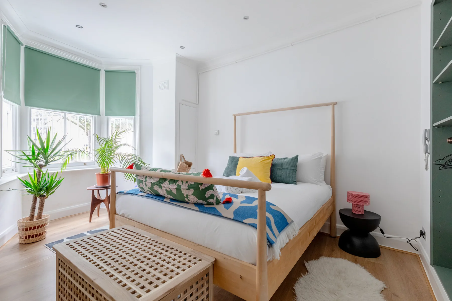 A bright bedroom with a wooden bed, colorful pillows, and green window blinds.
