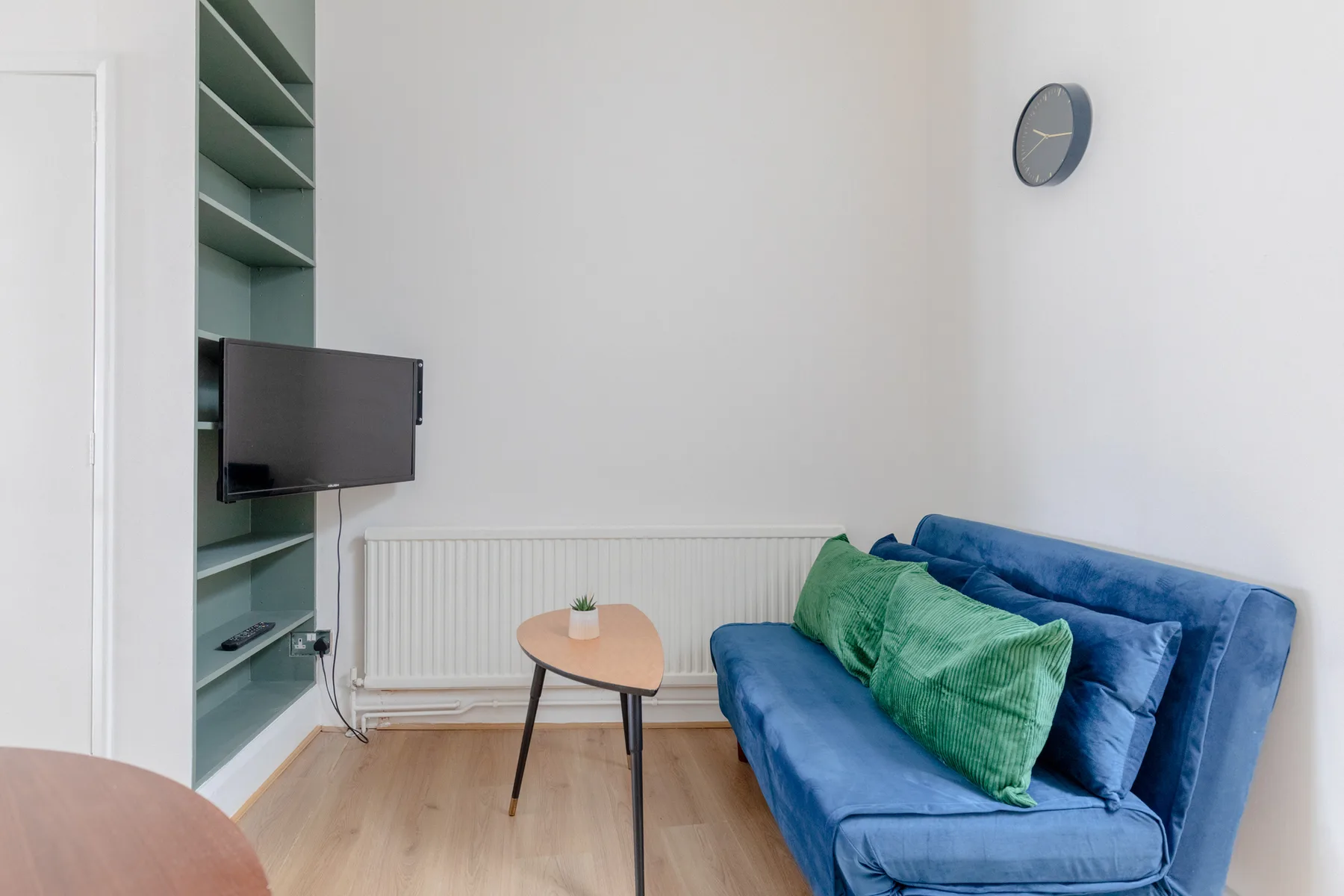Una sala de estar con asientos azules, una mesa pequeña y un televisor en la pared.