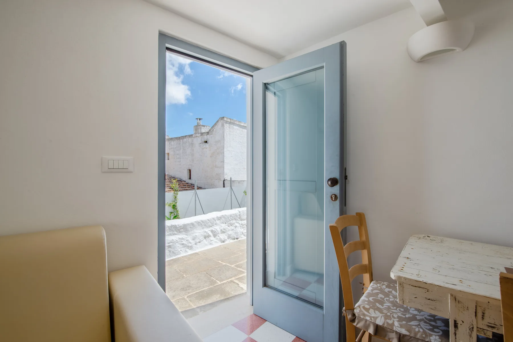 Una habitación luminosa con una puerta azul abierta que da a una pequeña terraza.