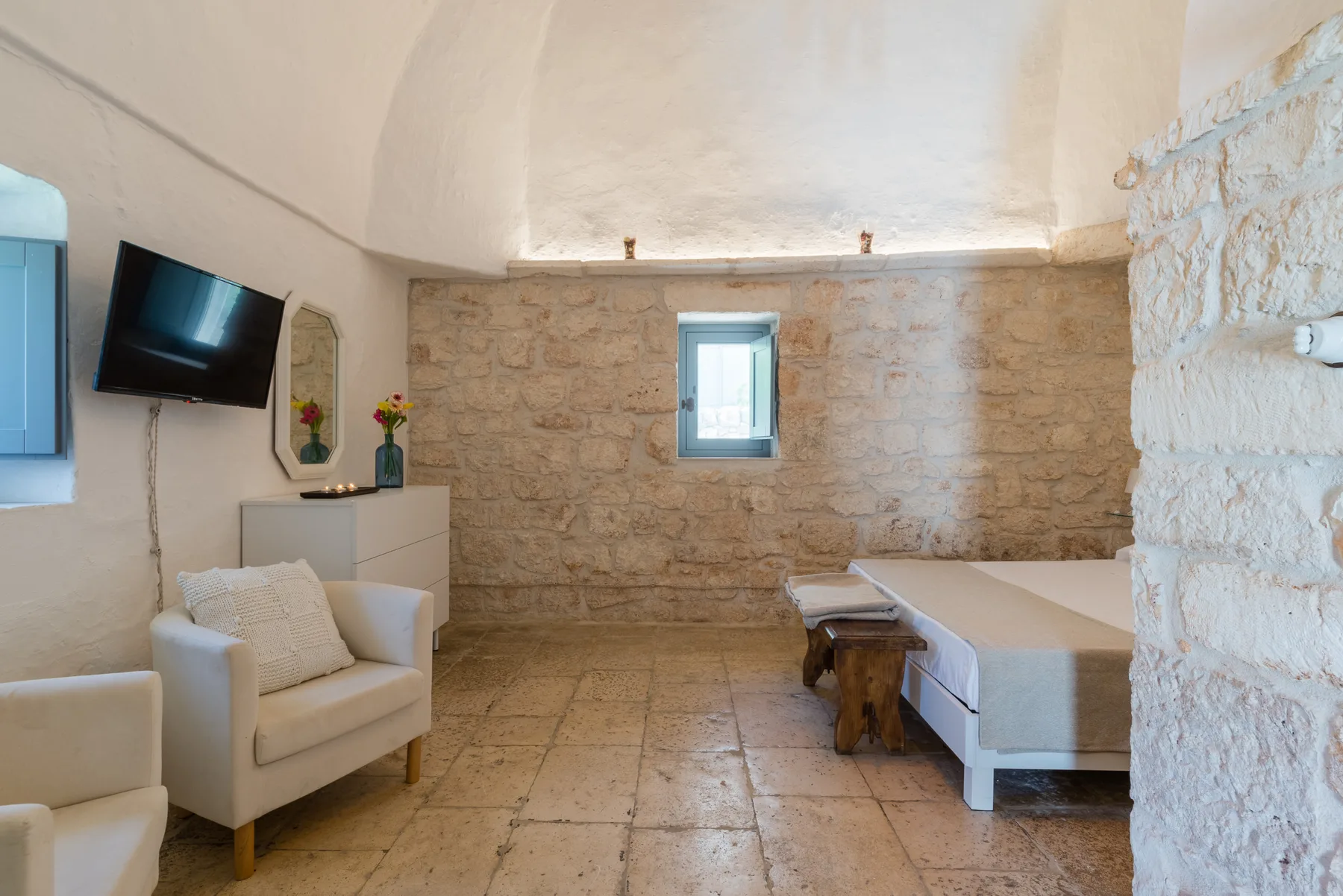 Un dormitorio con paredes de piedra, cama y asientos bajo un techo abovedado.
