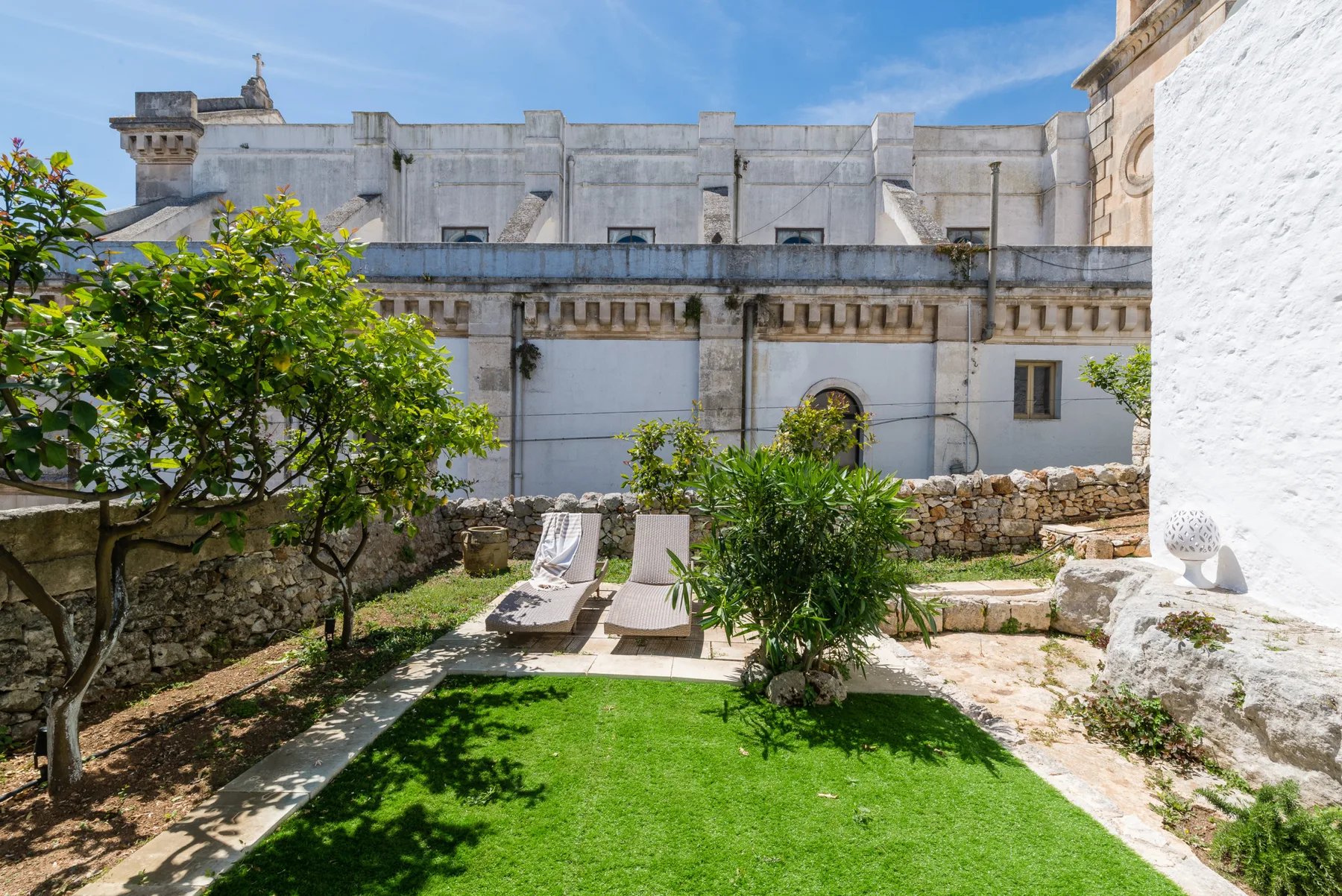 Un patio ajardinado con césped, árboles frondosos y un edificio de piedra clara.