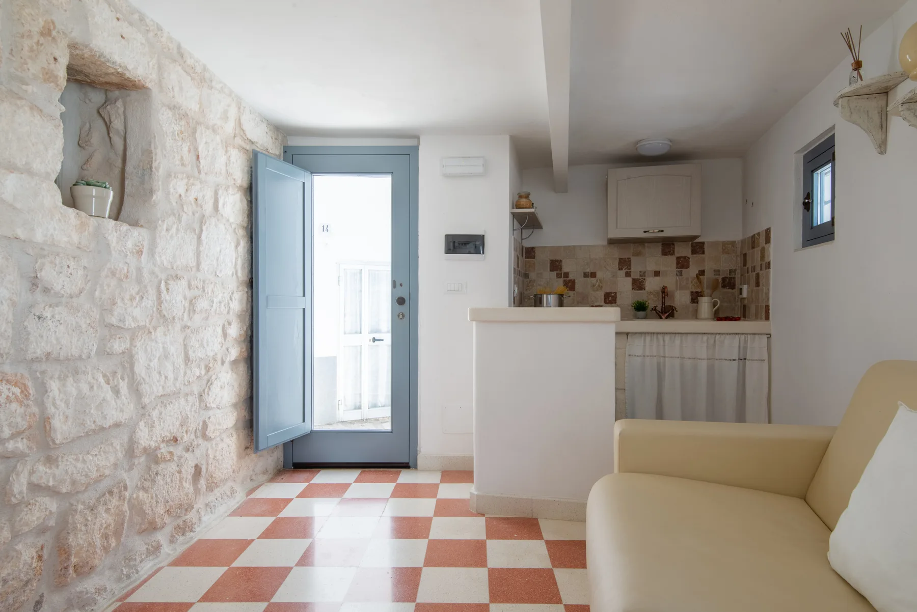 Un interior luminoso con una pequeña cocina, asientos claros y suelo de baldosas a cuadros.