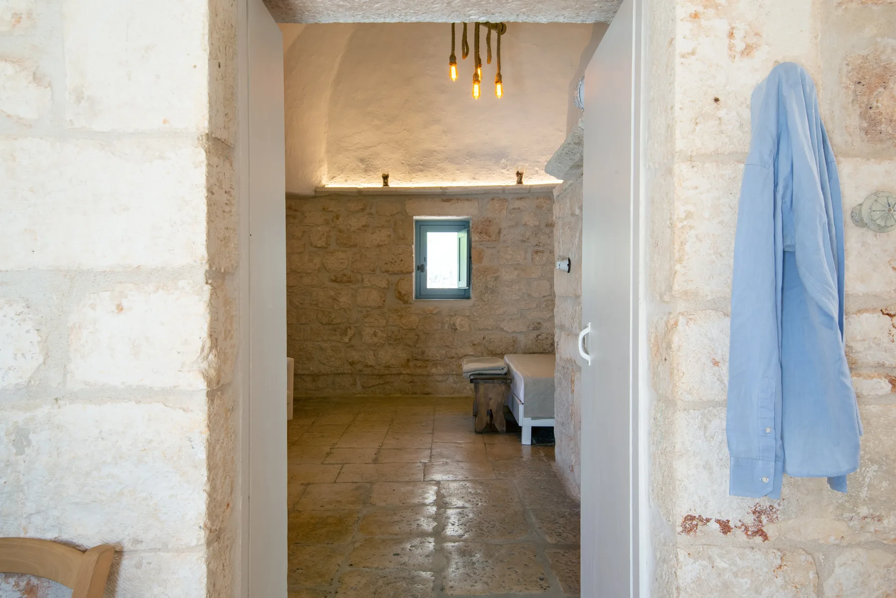 Un baño de piedra con una ventana pequeña y una bata azul colgada junto a la entrada.