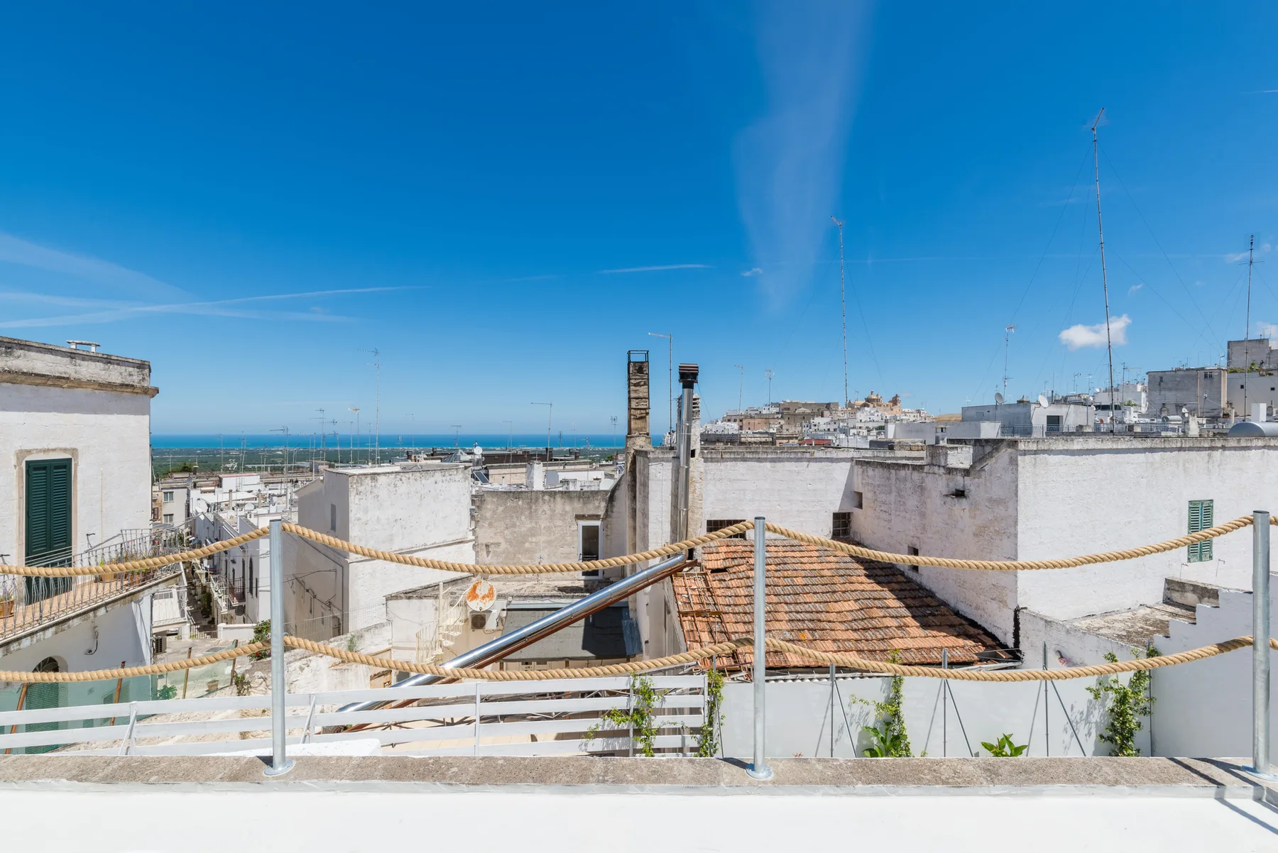 Una terraza en la azotea ofrece vistas de edificios blancos y del mar bajo un cielo azul despejado.
