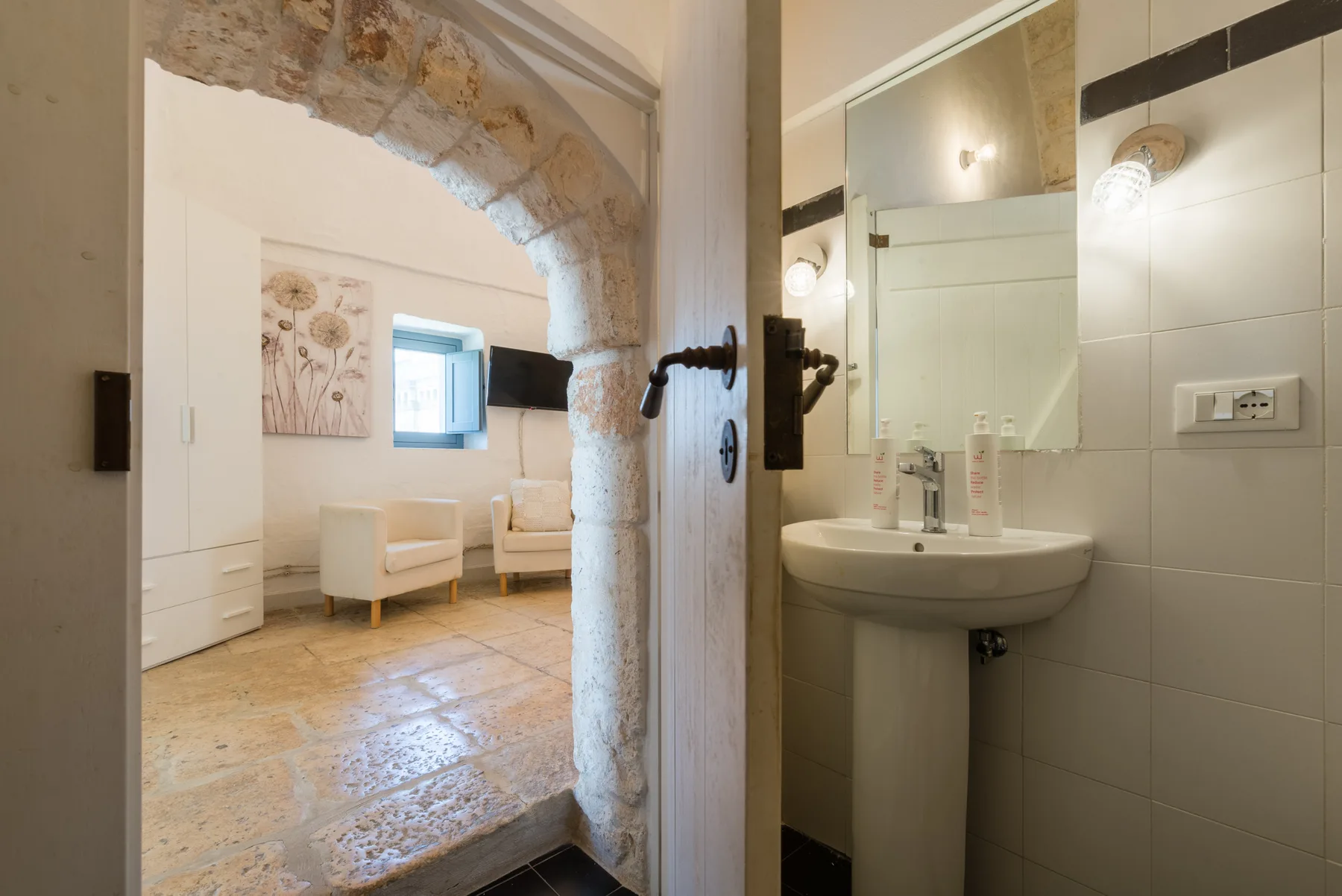 Un baño alicatado con lavabo se abre a una zona de estar mediante un arco de piedra.