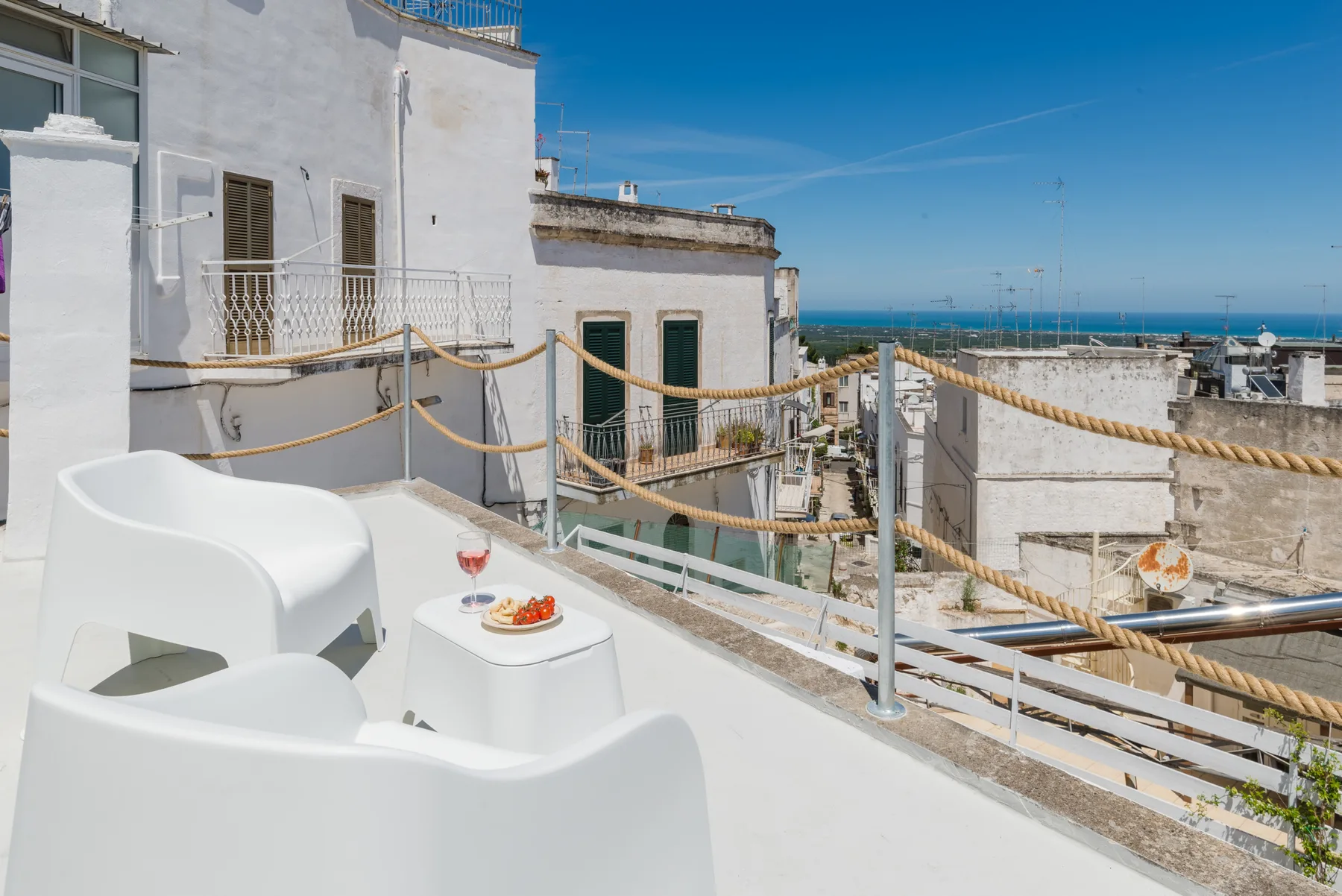 Una terraza en la azotea con asientos blancos da a edificios cercanos y al mar.