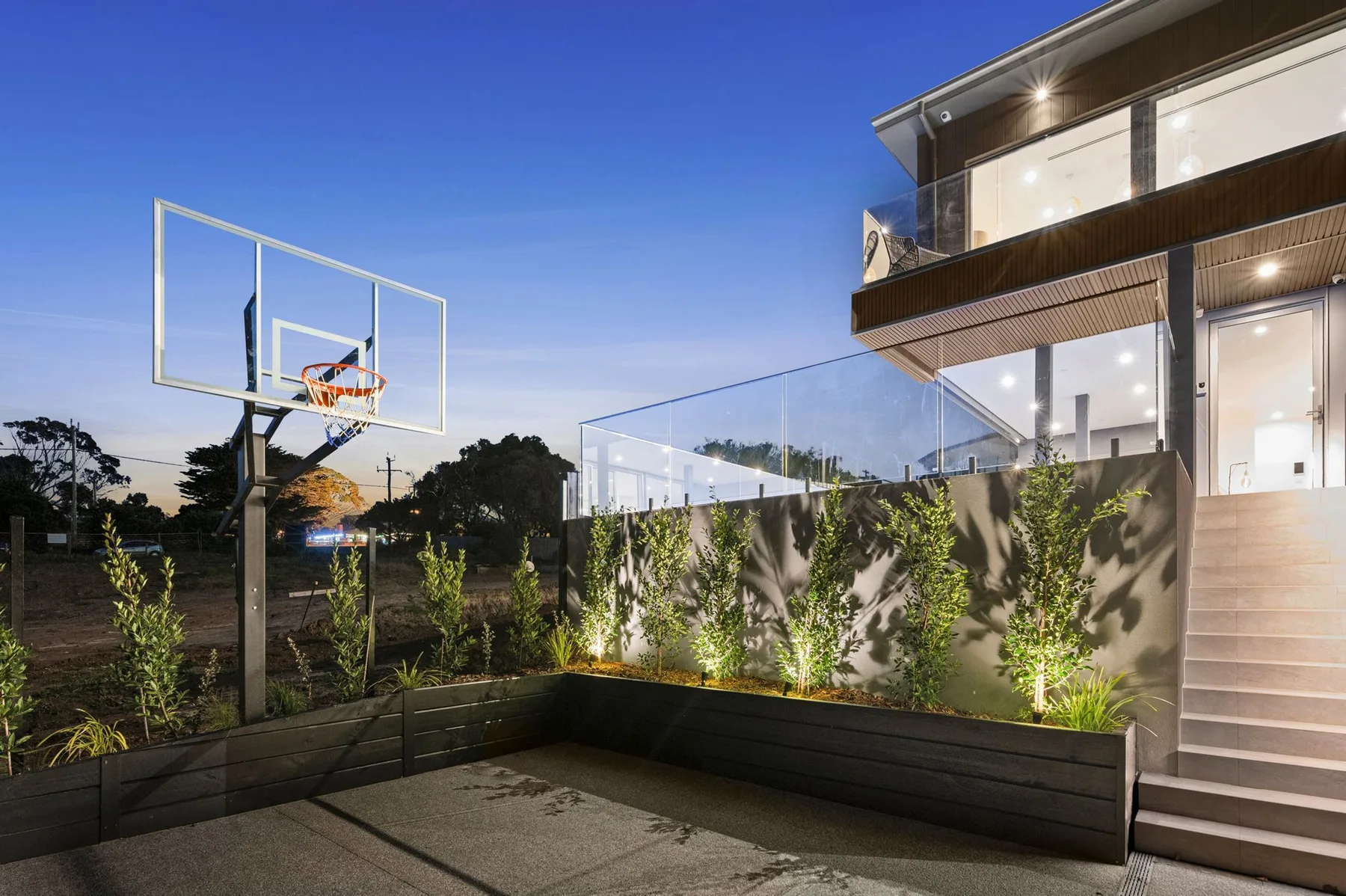 Una canasta de baloncesto exterior está junto a una casa moderna al anochecer.