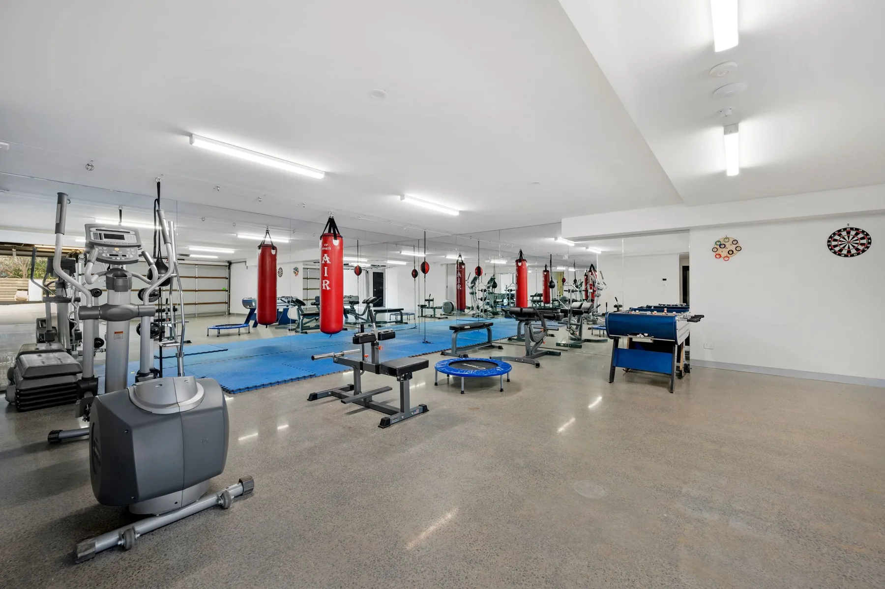 Un gimnasio amplio con equipos de ejercicio, bancos de pesas y colchonetas azules.
