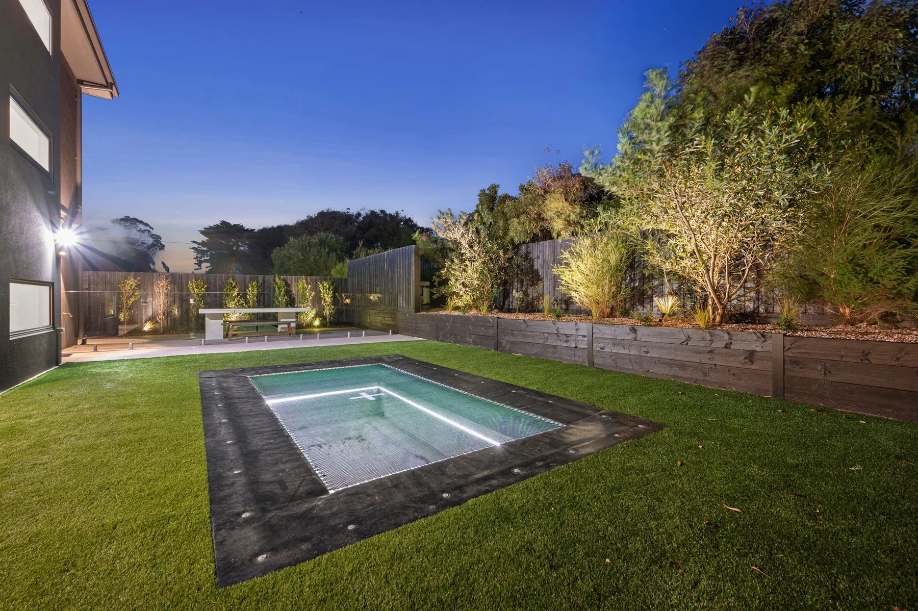 Una pequeña piscina al aire libre está en un jardín con césped junto a una casa.