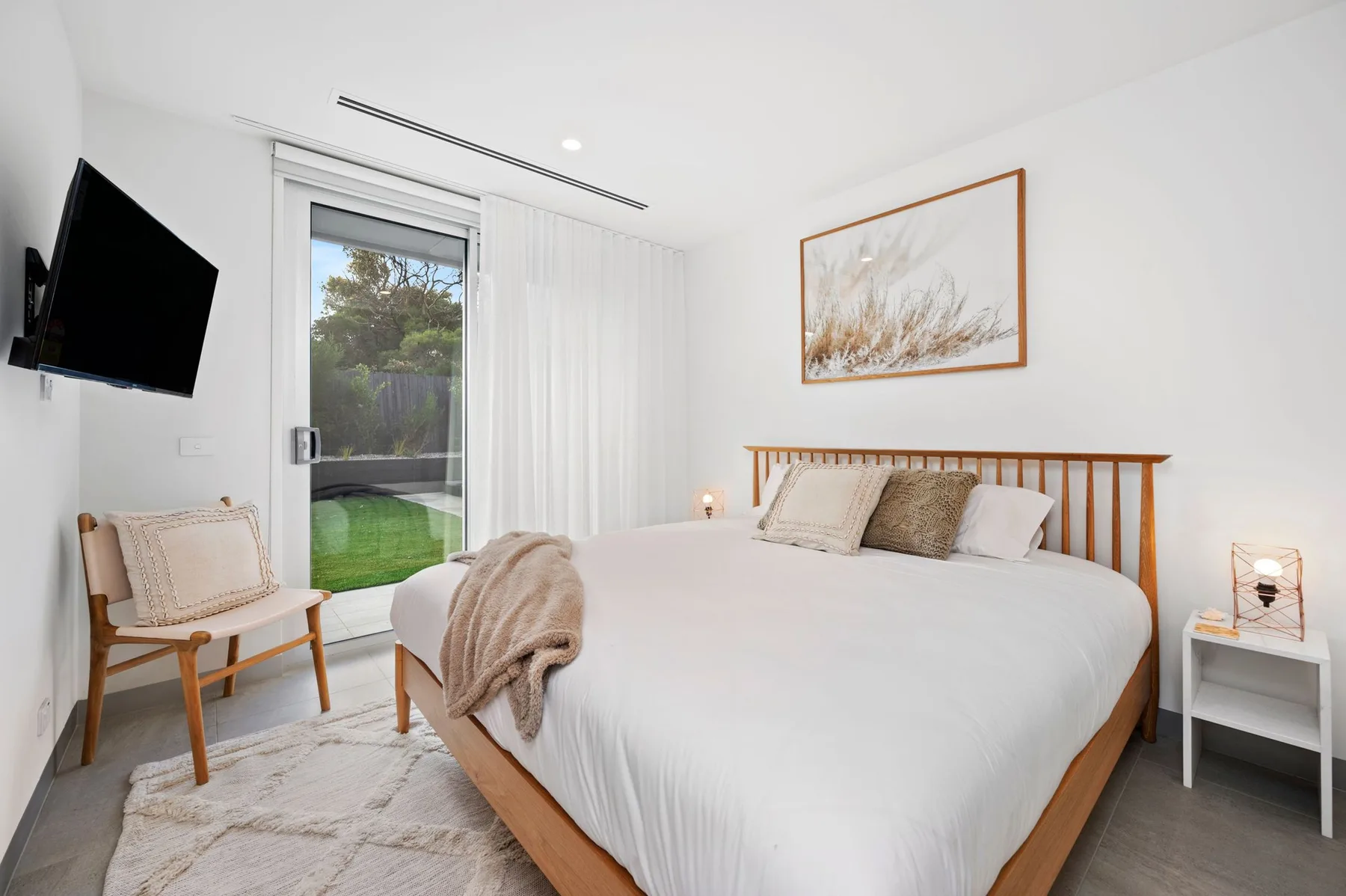 Un dormitorio luminoso con una cama grande, una silla y puertas de vidrio que dan a un jardín.