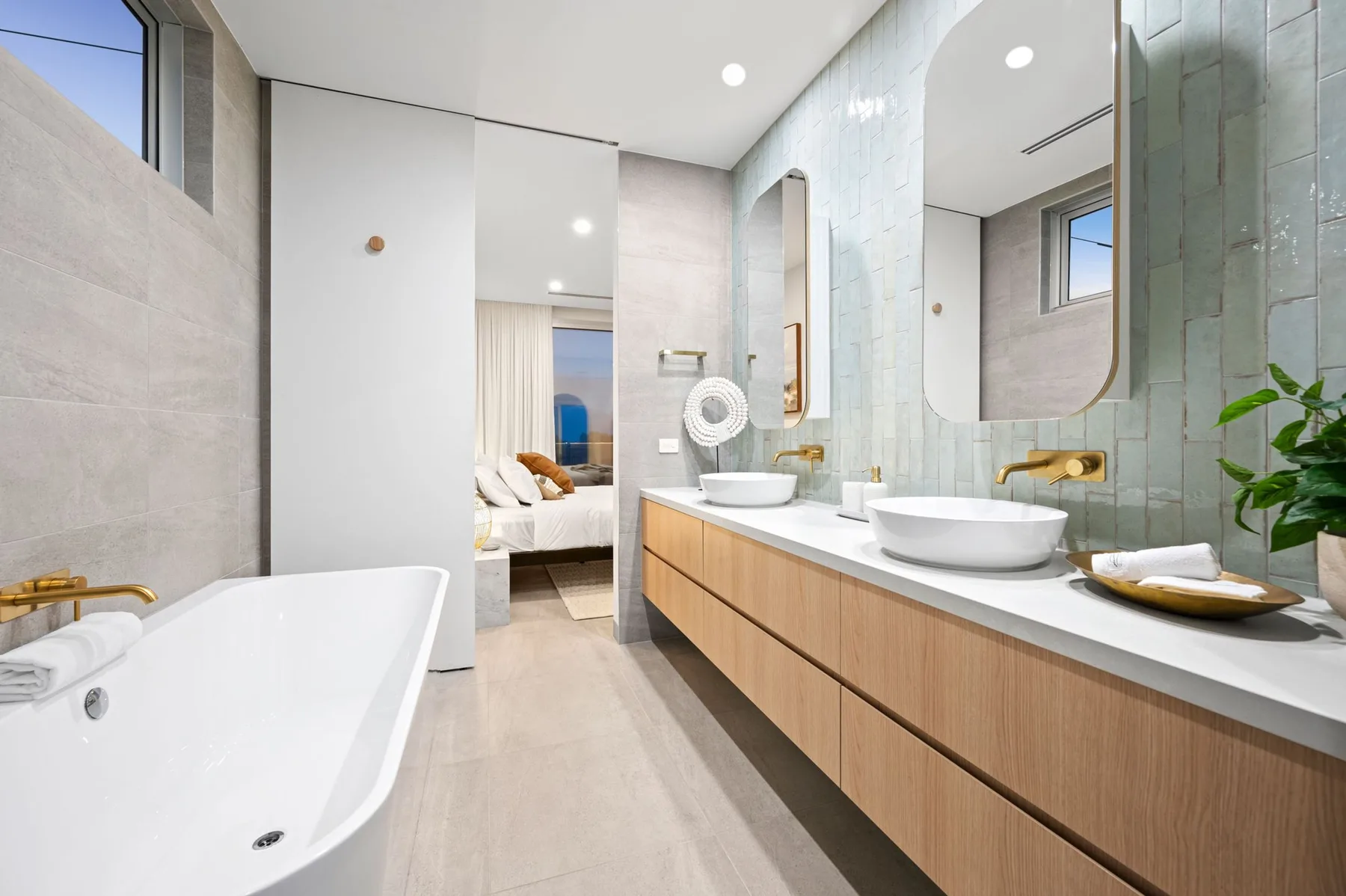 Un baño luminoso tiene una bañera y un largo lavabo con dos lavabos.