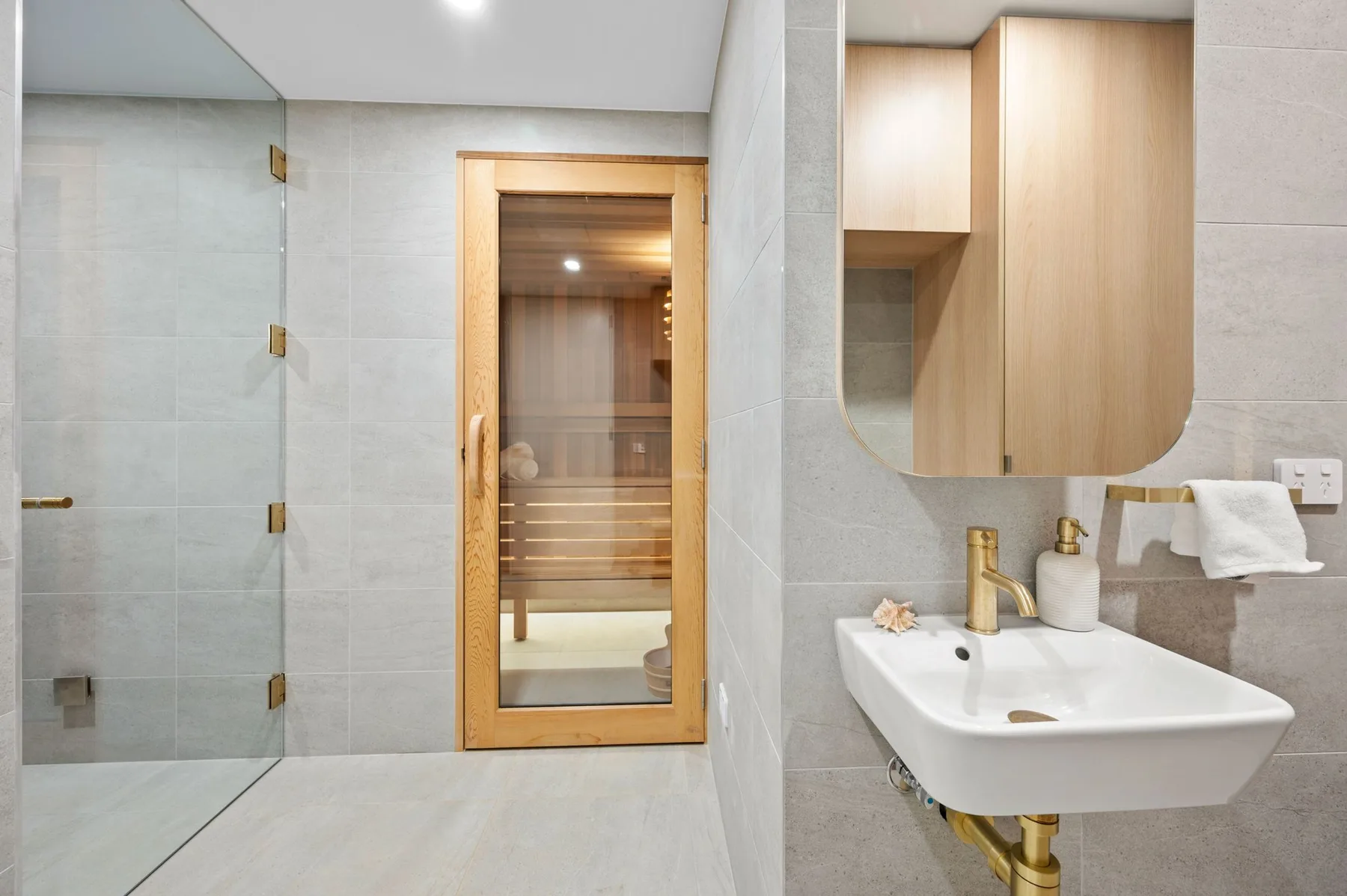 Un baño con ducha de vidrio, lavabo y sauna de madera.