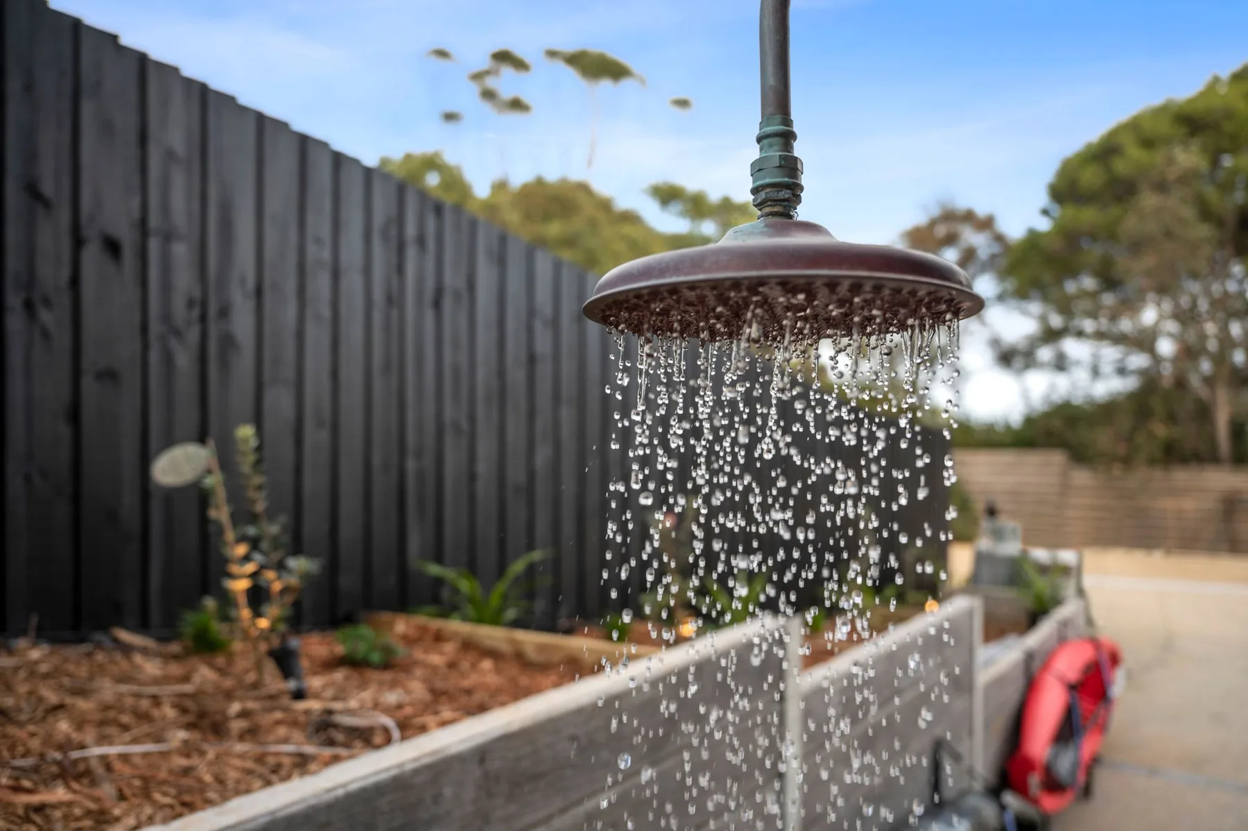 Una ducha exterior rocía agua junto a un jardín cercado.