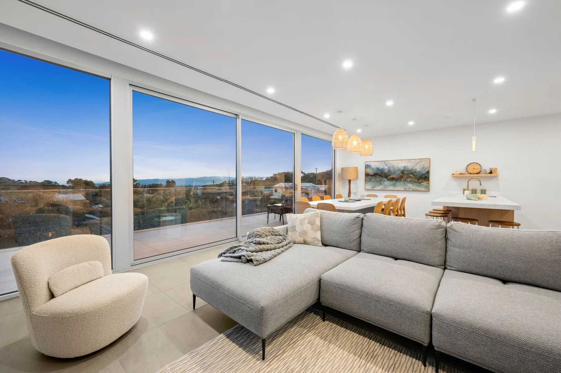 Una sala luminosa tiene una zona de asientos junto a grandes ventanales con vistas al paisaje.