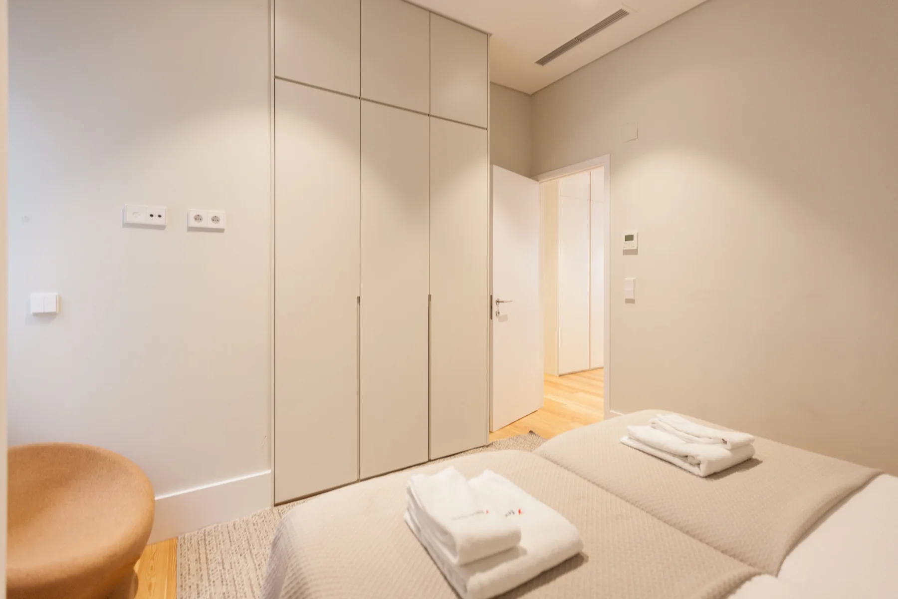 Un dormitorio luminoso con una cama, toallas dobladas y armarios empotrados.