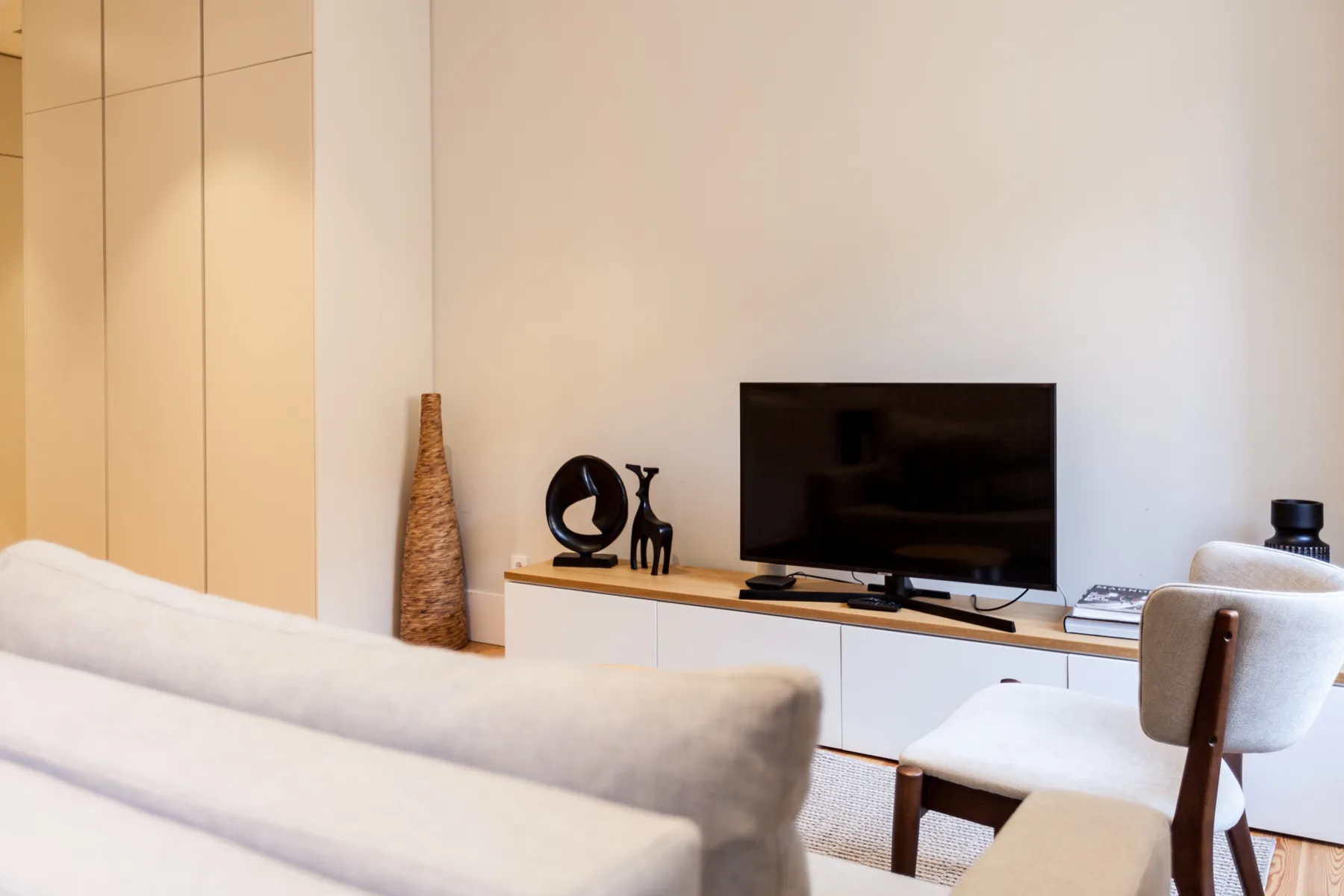Una sala de estar con un televisor sobre un mueble bajo y asientos claros.