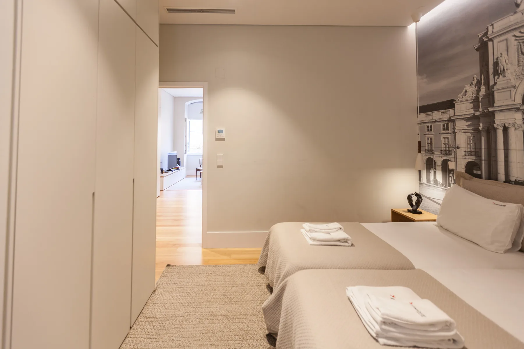 Un dormitorio con dos camas, toallas dobladas y un gran mural arquitectónico en la pared.