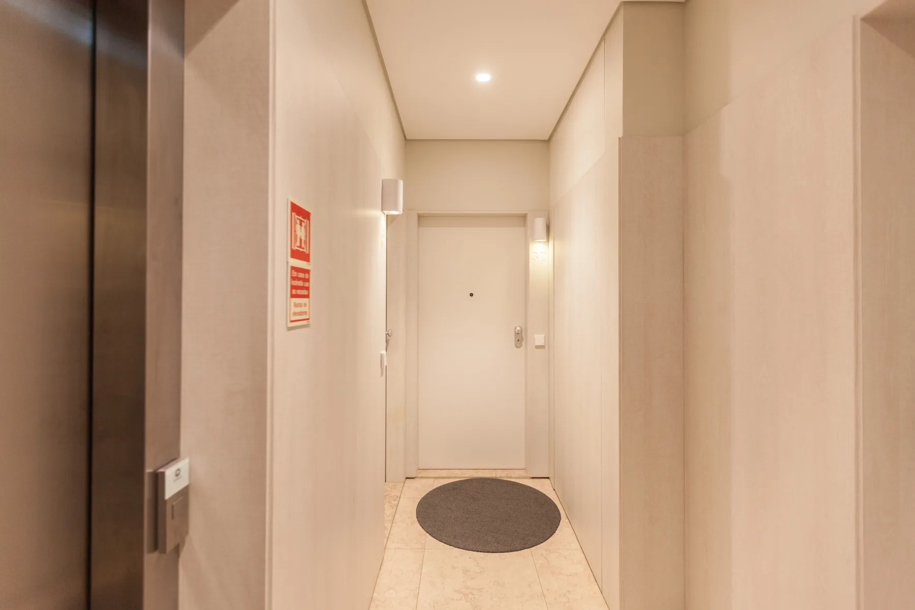 Un pasillo de entrada luminoso con una puerta cerrada y una alfombra redonda.