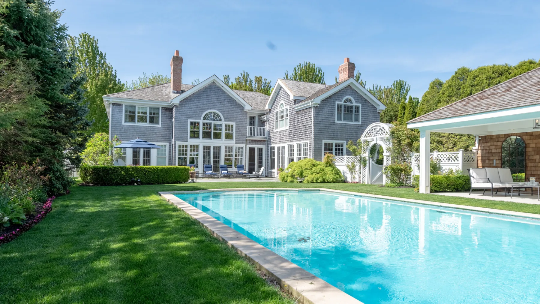 A swimming pool and lawn sit in front of a large gray house.
