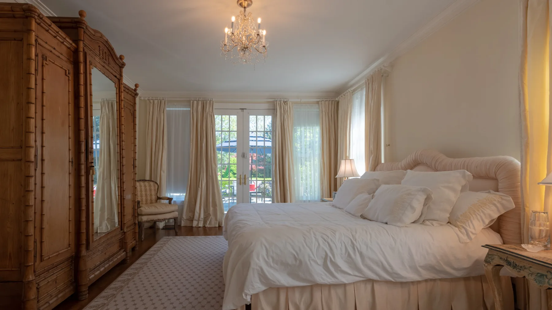 A bedroom with a large bed, wardrobe, and tall curtained windows.